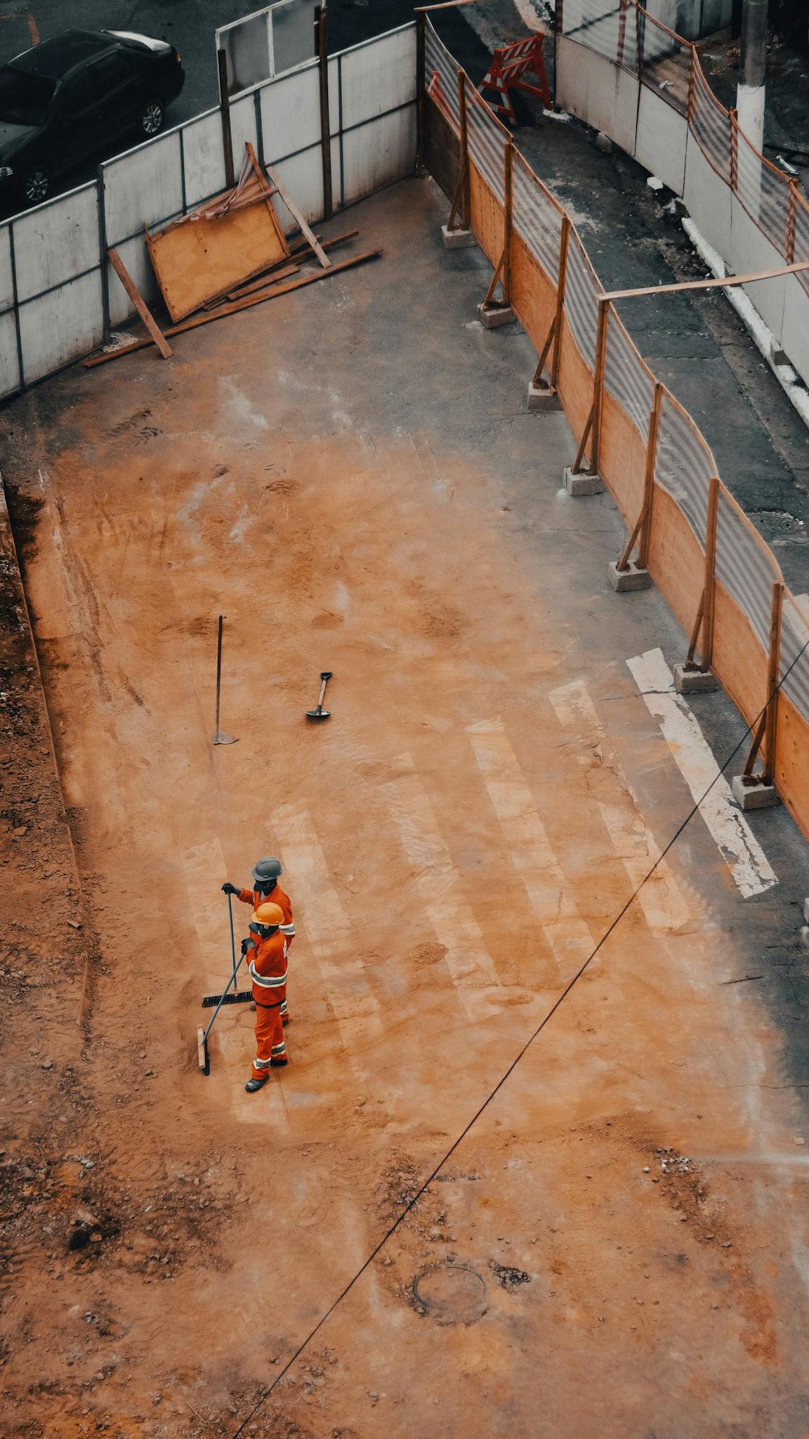 Construction worker on site, viewed from above, wearing safety gear. Daylight setting with visible equipment.