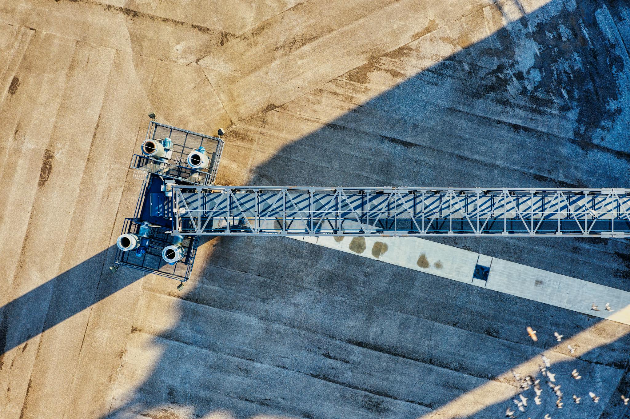 Drone capture of an industrial crane casting shadows on a construction site in bright sunlight.